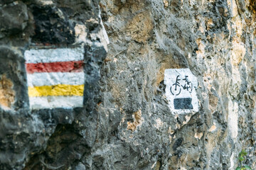 Painted trail and cycling route markers on a rugged stone wall along a mountain path. Outdoor navigation, sustainable tourism, trail safety, eco-friendly travel