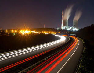 Fototapeta premium Night highway with vivid light trails and a glowing power plant, showcasing modern industry and transport under a dark sky.