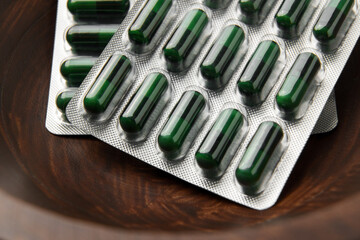 Green medicional capsules blister pack in wooden eco-friendly bowl. Macro shot