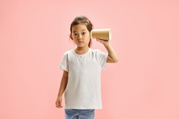 Curious little child girl in white t shirt use paper cup to eavesdrop it's better to hear what...