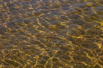 Golden closeup abstract of wave water with sunshine reflection on background.