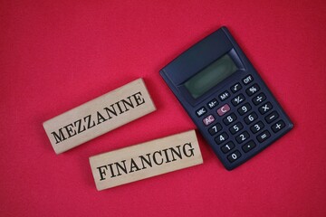 Finance Concept With Calculator and Mezzanine Financing Wooden Blocks Display on a red background