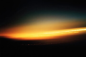 A vibrant sunset viewed from above, with a dramatic band of gold and orange light across a dark sky