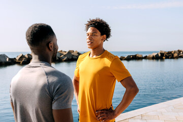 Two Hispanic men engage in outdoor workout by the waterfront during a sunny day