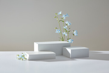 White geometric podiums with gentle blue blossoms arranged on a beige background, ideal for clean...