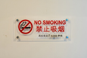 No smoking sign with bilingual English and Chinese text displayed on a white wall indicating a fine...