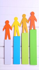 Colorful paper figures stand on graduated height bars, symbolizing growth or teamwork