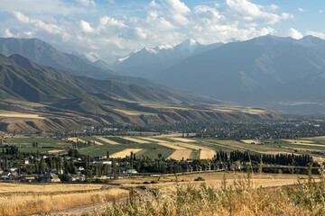 Kyrgyzstan autumn landscape. Village, agricultural fields and high mountains. Rural scene