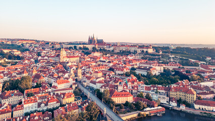 A breathtaking view of Prague at sunrise reveals the city's iconic skyline. The Vltava river gracefully flows alongside historic buildings, with the Charles Bridge and castle in the background.