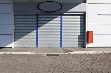 Store at the roadside with entrance metal rolling shutters closed and divided by shadow. Tiled sidewalk in front. Background for copy space.