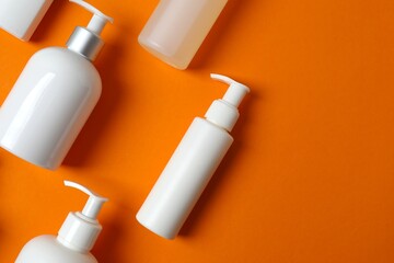 Various skincare white bottles on orange background, top view