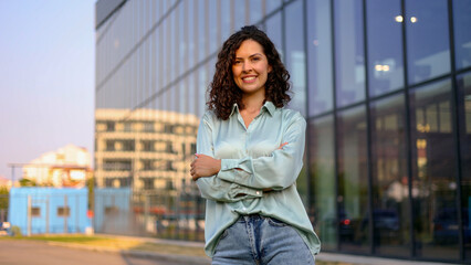 Portrait of a successful businesswoman smiling confidently with arms crossed, standing in front of...