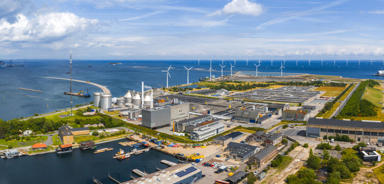 Aerial view of Copenhagen, Denmark, showing a waste to energy plant, industrial buildings, coastal wind turbines, and ships on the blue sea.