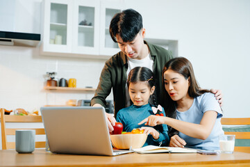 Asian family waves and smiles during a joyful video call at home. Parents and daughter connect digitally, sharing love