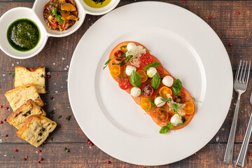 Plated tomato and mozzarella arrangement garnished with basil and herbs