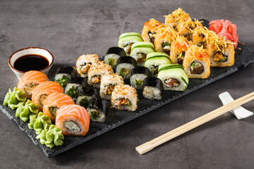 Assorted sushi rolls served on a slate plate with wasabi, soy sauce, and ginger