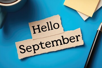 Hello september text on blue desk. coffe mug, fountain pen and note sheets on background.