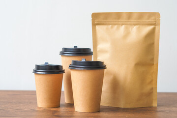 Coffee paper cup and Kraft paper bag on wooden table. Mockup for you designs.