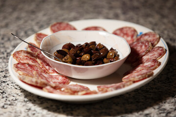 piatto con fette di salame e una scodella di olive, su un tavolo di marmo