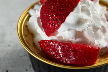 A closeup view of a container of flan, topped with strawberries and whipped cream.