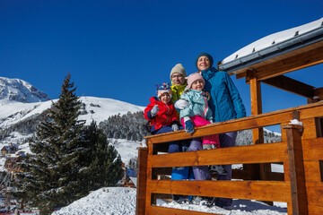 Smiling family stands on wooden balcony in bright winter jackets