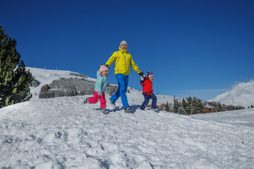 Dad in neon green leads two kids running across a snowy field