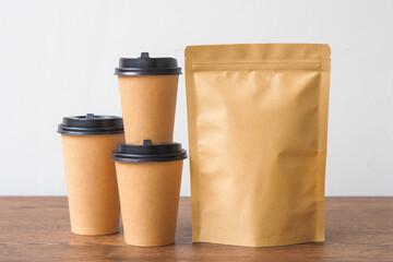 Coffee paper cup and Kraft paper bag on wooden table. Mockup for you designs.