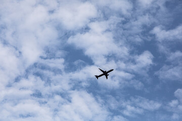 Airplane silhouette flying through blue sky with white fluffy clouds