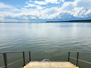 Scenic Calm Lake View with Clear Sky and Cloud Reflections on Water Near Wooden Steps