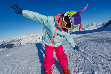 Child skiing in bright gear, posing happily on snowy slopes