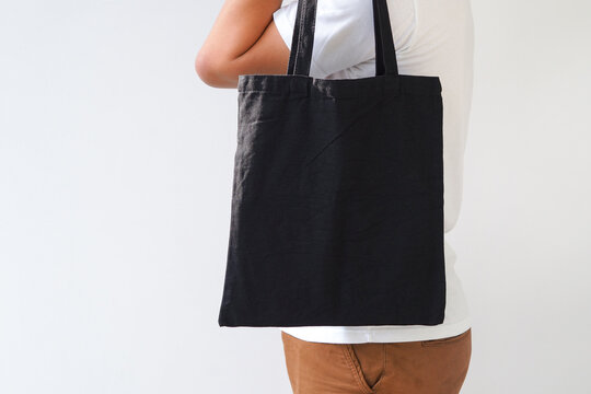 Young man hand holding black canvas tote bag on white background. Reusable eco bag for shopping. Eco friendly concept. Mockup for you designs.