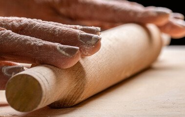 Closeup of man rolling dough with rolling pin for homemade bakery at table. Man rolling out dough...