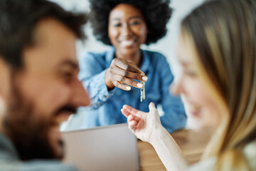 Portrait  of real estate agent or youn businesswoman giving keys to couple of customers in office