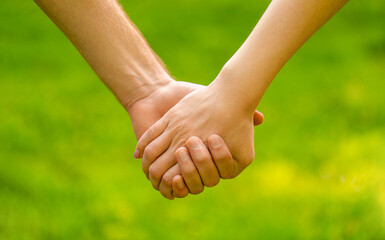 Couple holding hands in the park. Couple hold hand in the autumn or summer park. Closeup of loving couples holding hands while walking. Female and male hand together