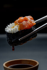 Sushi on chopsticks dipped in soy sauce on a dark background