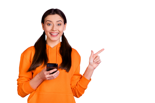 Portrait of positive cheerful youth girl blogger hold her cellphone point indexf inger on copyspace repost news wear orange trendy stylish sportswear isolated over violet purple color background
