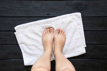 Clean female feet after washing stand on a white towel on a wooden floor, hygiene and foot care
