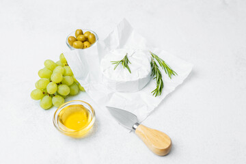Cheese platter with herbs, olives, and grapes arranged on a white surface