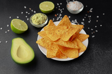 Plate of nacho chips with guacamole, lime, avocado and salt on dark background