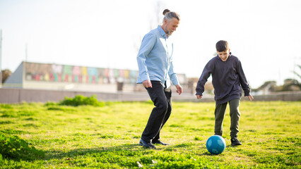 Grandfather and grandson playing soccer on green grass under bright sky