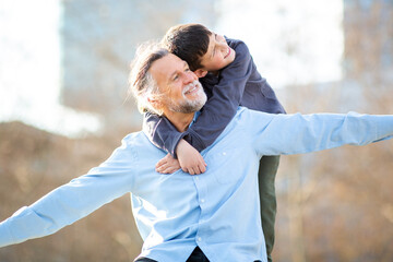 Grandfather and grandson playing airplane arms game while smiling in the park