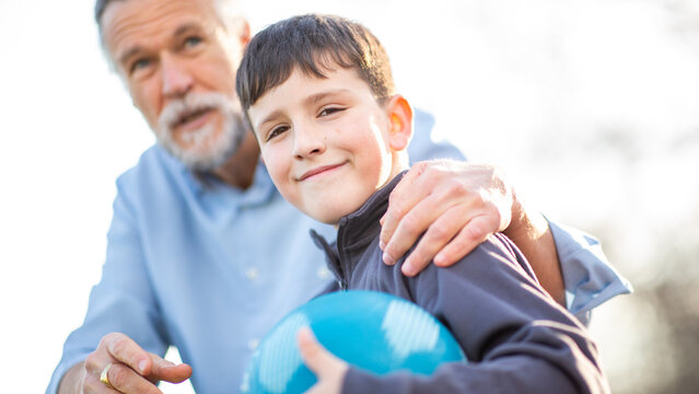 Smiling boy holding blue ball as grandfather lovingly wraps arm around him