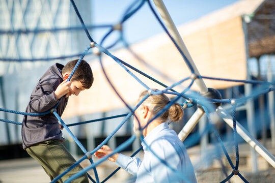 Boy climbing rope playground structure with grandfather offering support