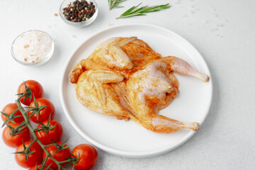 Raw marinated quail on white plate with tomatoes, salt, pepper and rosemary