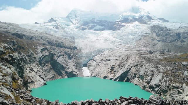Aerial ascending shot closely follows a rugged rocky ridge leading toward the bright turquoise waters of Laguna 513 in the Peruvian Andes.