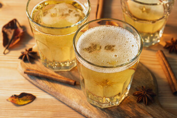 Golden spiced apple cider with cinnamon and star anise in faceted glasses on rustic board, warm sun sets autumn mood for friends.