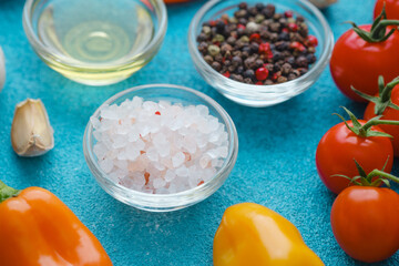 close up of black peppercorns, salt, tomatoes and peppers on blue background