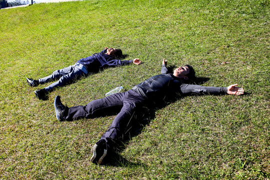 Two Men Lying On Their Backs On The Grass, Tired After Exercising, Resting Under The Sky