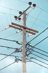 Concrete utility pole with tangled electric wires and insulators against a clear blue sky.
