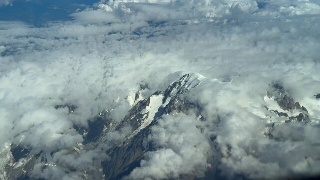 An aerial view of the Mont Blanc summit covered with few snow in a summer morning, veiled by ethereal clouds. Shot taken from a jet cokpit flying 7000m high.